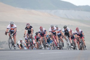 UCA Bike For Kids Stage Race The Masters men's field rounds a corner with the Kennecott Copper Mine in the background.